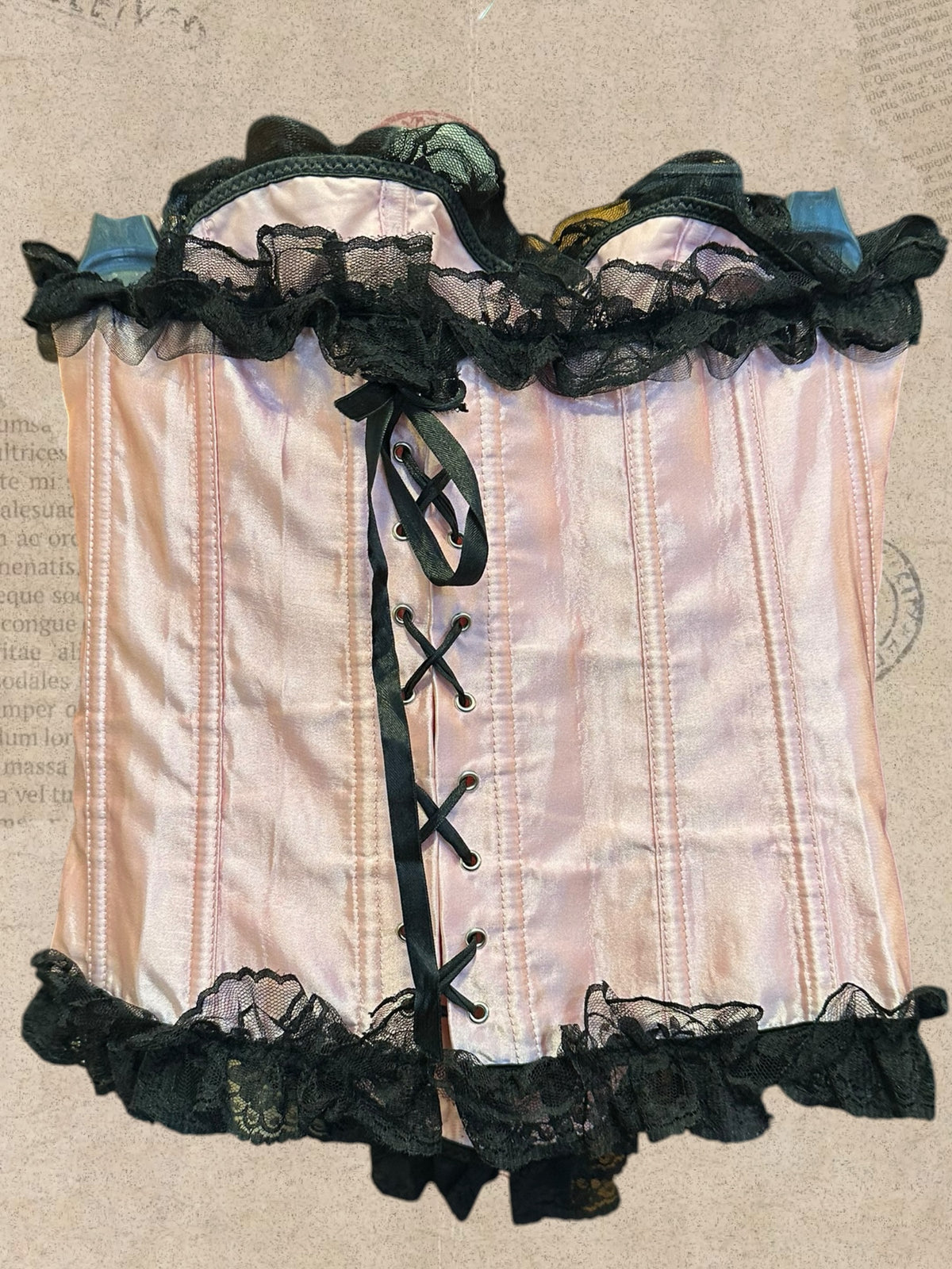 Romantic blush pink satin corset with black lace ruffles. Features adjustable ribbon lacing and delicate bow details. A dreamy Victorian-inspired statement piece.