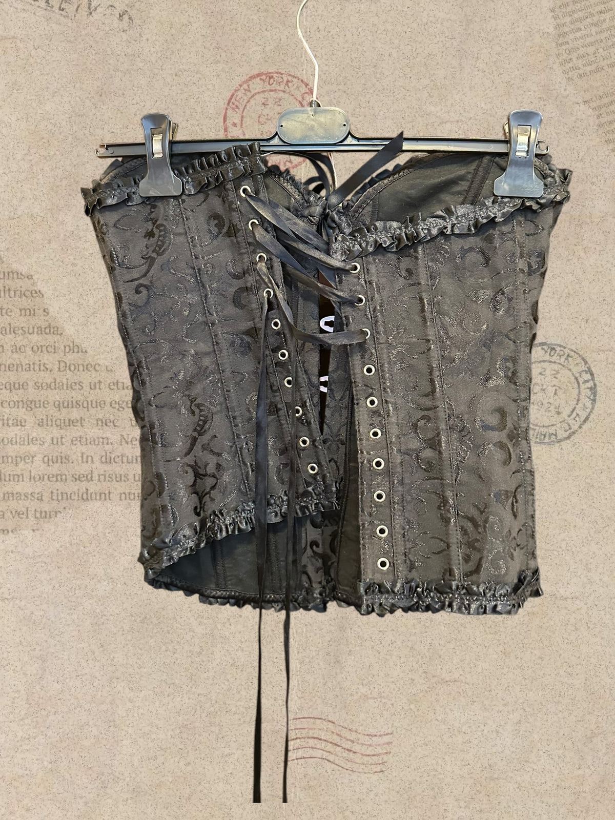 Black floral brocade corset with ruffled trim. Front hook closures and satin bow. Elegant gothic style.