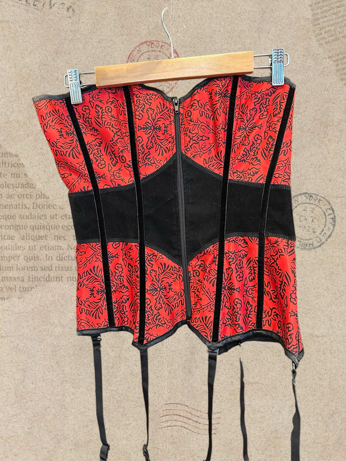 Gothic red and black corset with intricate floral patterns and a structured silhouette. Features adjustable lace-up back, front zipper, and garter straps. A bold Victorian-inspired statement piece.