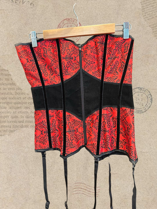 Gothic red and black corset with intricate floral patterns and a structured silhouette. Features adjustable lace-up back, front zipper, and garter straps. A bold Victorian-inspired statement piece.