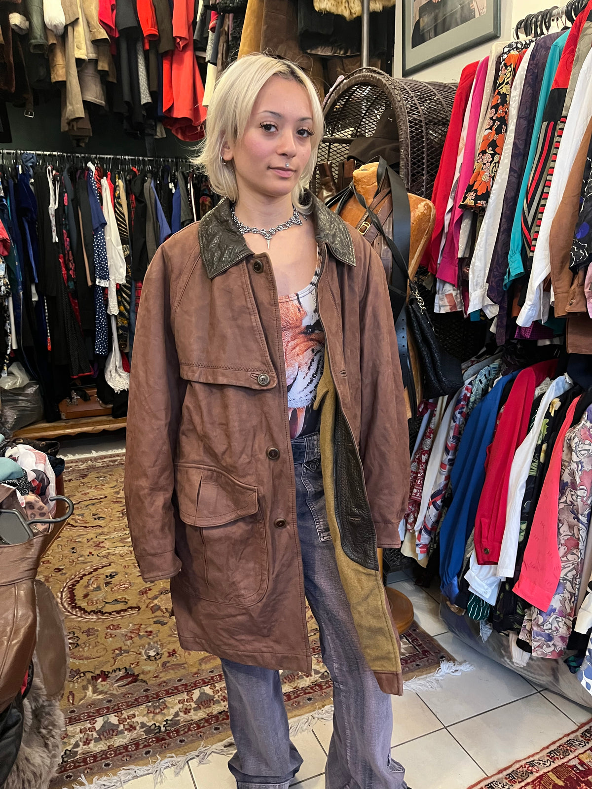 Vintage brown leather coat featuring a contrasting dark leather collar and utility-inspired patch pockets. Designed with a relaxed longline silhouette, button-front closure, and distinctive cape-style back panel