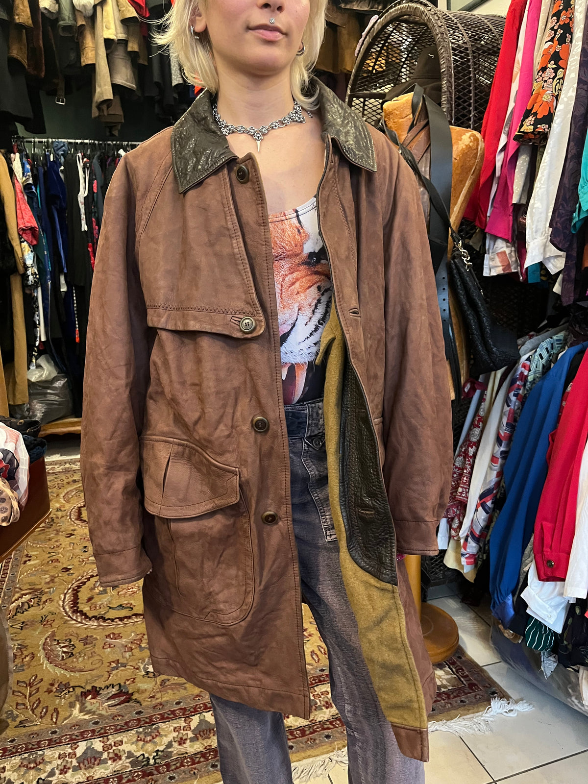 Vintage brown leather coat featuring a contrasting dark leather collar and utility-inspired patch pockets. Designed with a relaxed longline silhouette, button-front closure, and distinctive cape-style back panel