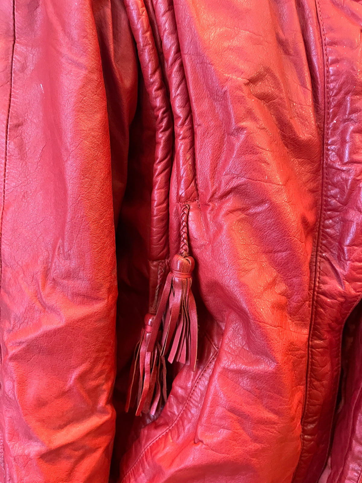 Statement red leather jacket featuring sculptural braided detailing and playful tassel accents. A bold vintage piece with a relaxed silhouette, zip-front closure, and unmistakable 80s-inspired attitude.