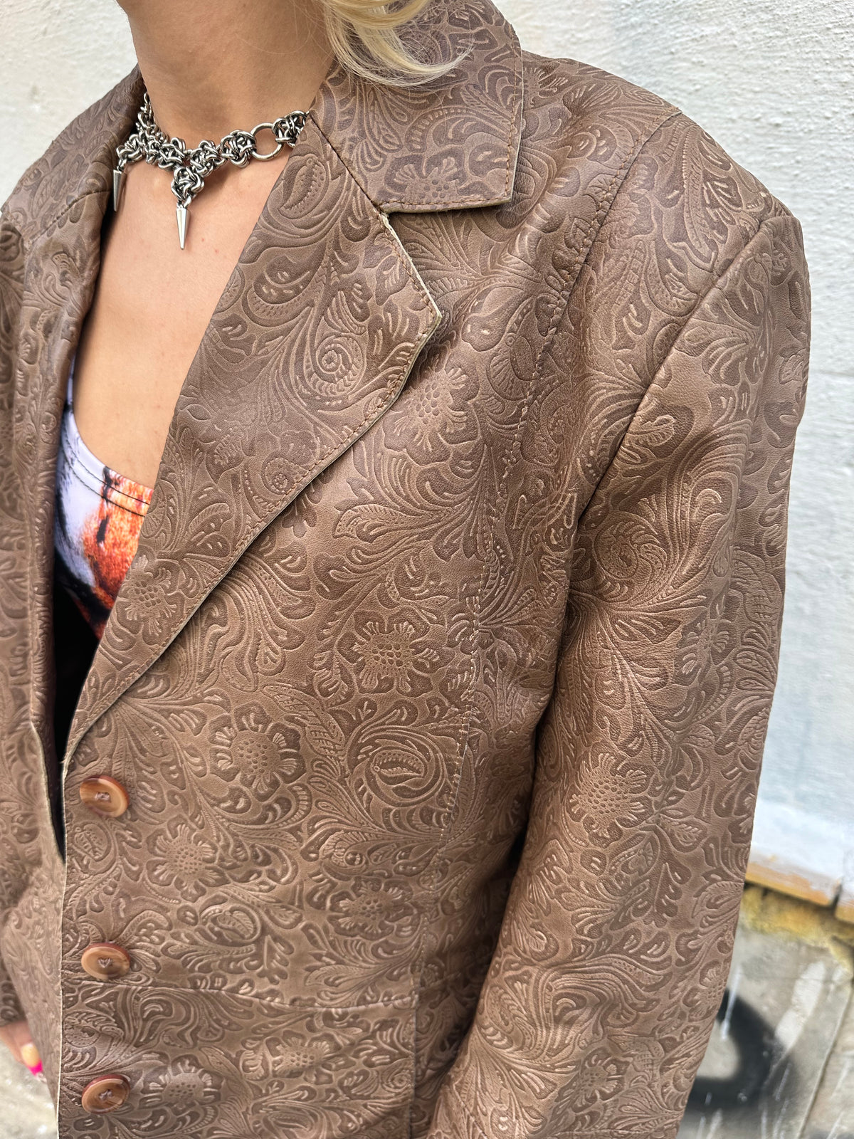 Vintage brown leather blazer with an intricate embossed floral pattern and classic button front.
A unique statement piece with tailored lines and rich textured detailing.
