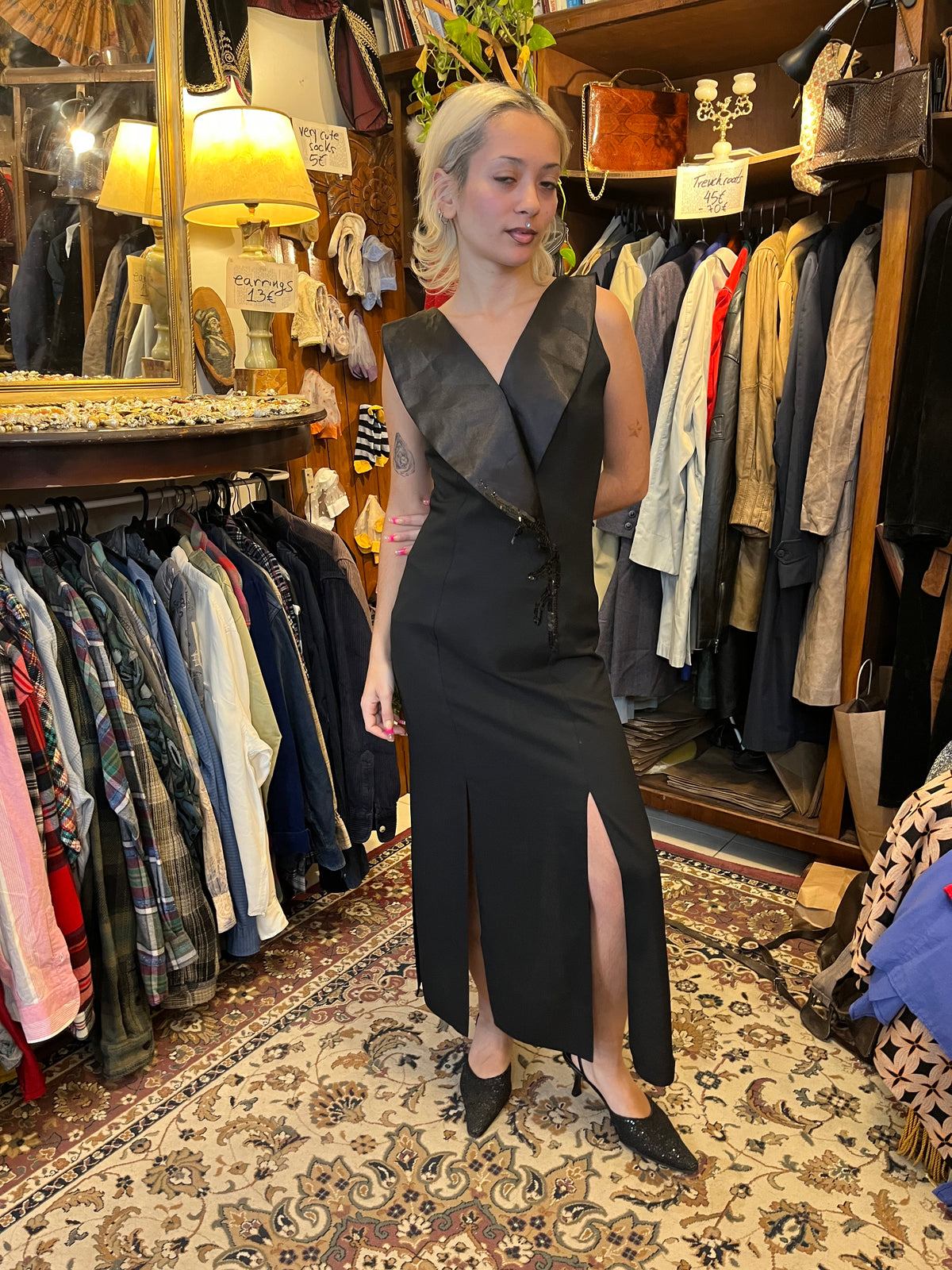 Elegant black maxi dress with a dramatic oversized V-neck collar and a sleek fitted silhouette. Finished with sequin detailing at the waist and bold front slits for a sophisticated statement look.