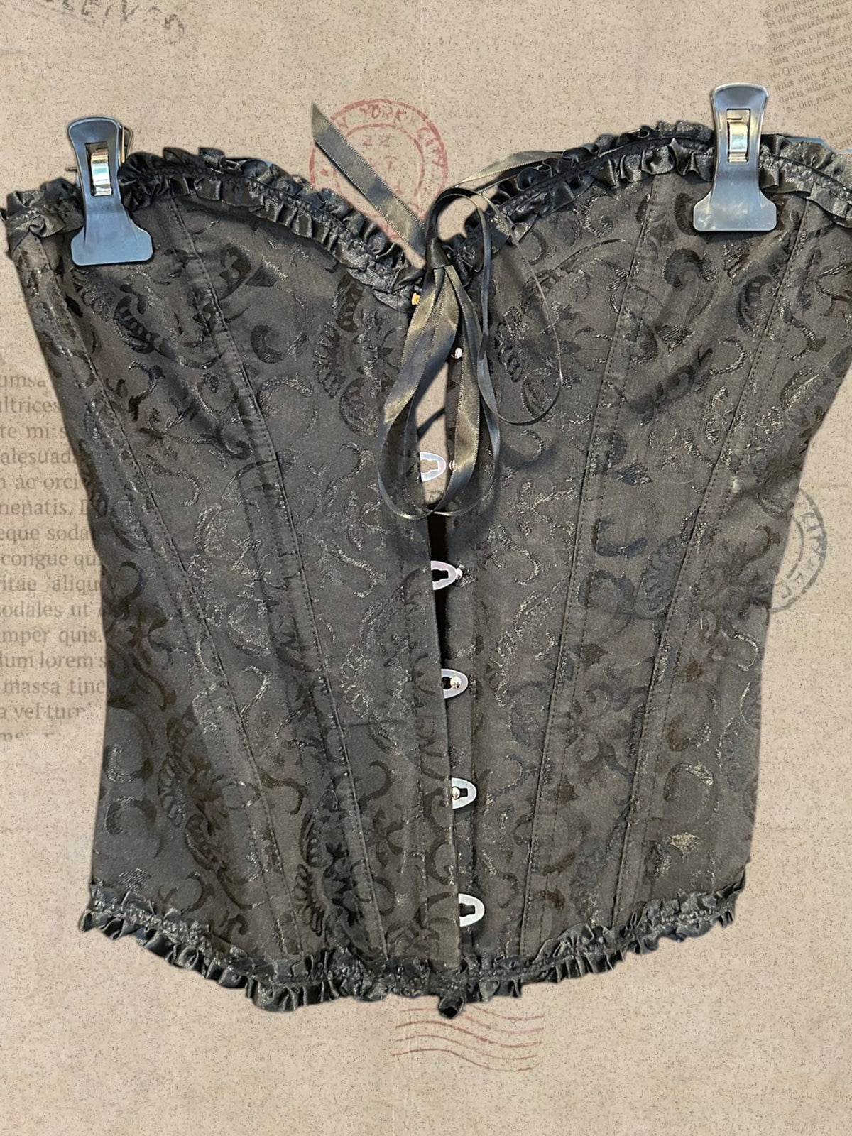 Black floral brocade corset with ruffled trim. Front hook closures and satin bow. Elegant gothic style.