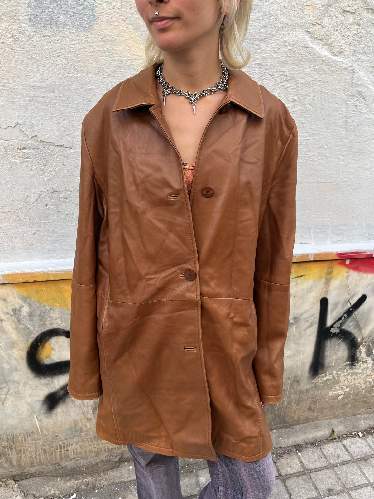 Vintage caramel-brown leather coat with a clean, minimalist silhouette and softly structured fit. Features a classic pointed collar, tonal button closure, subtle side pockets, and a beautifully aged leather finish.