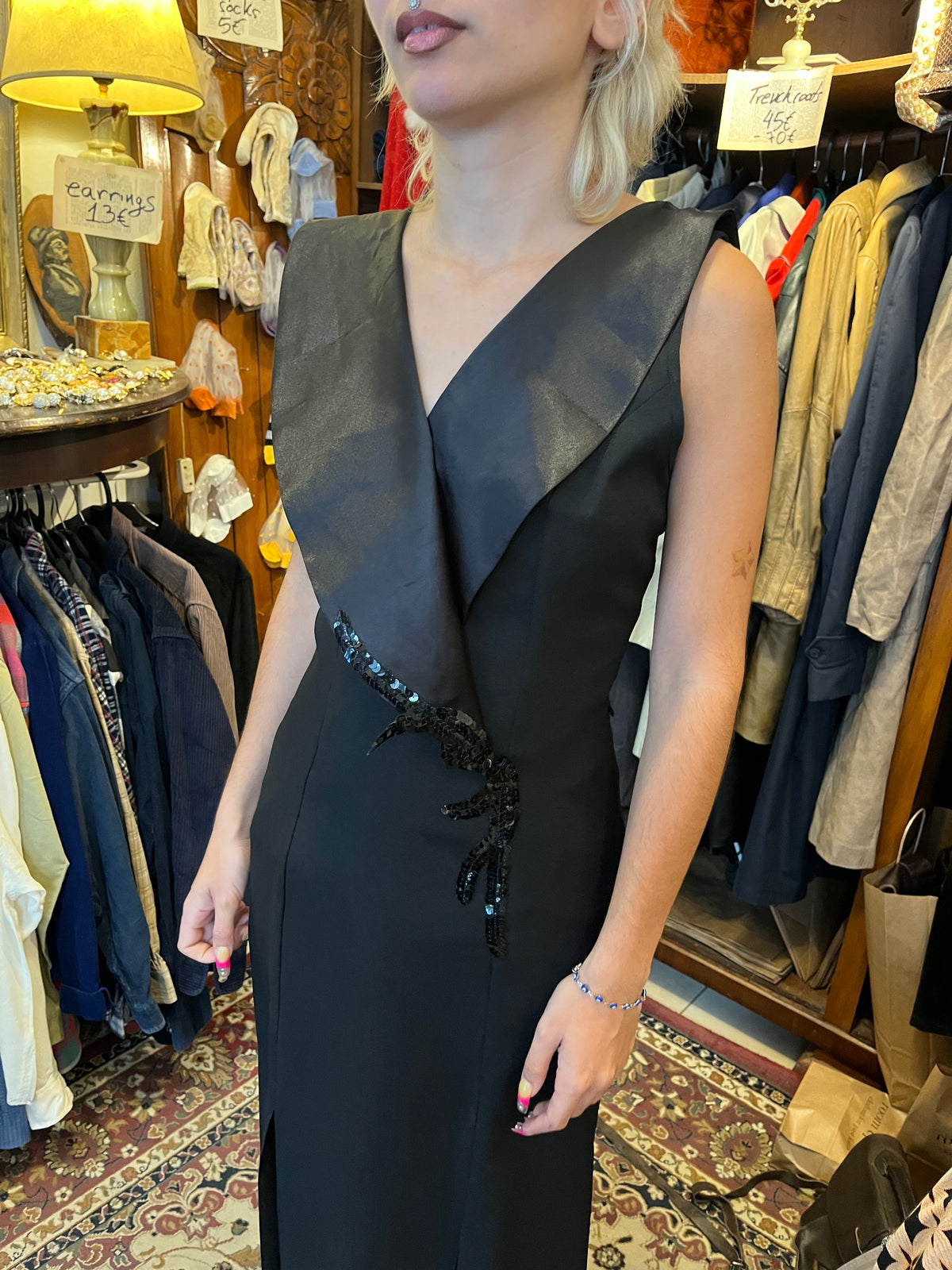 Elegant black maxi dress with a dramatic oversized V-neck collar and a sleek fitted silhouette. Finished with sequin detailing at the waist and bold front slits for a sophisticated statement look.