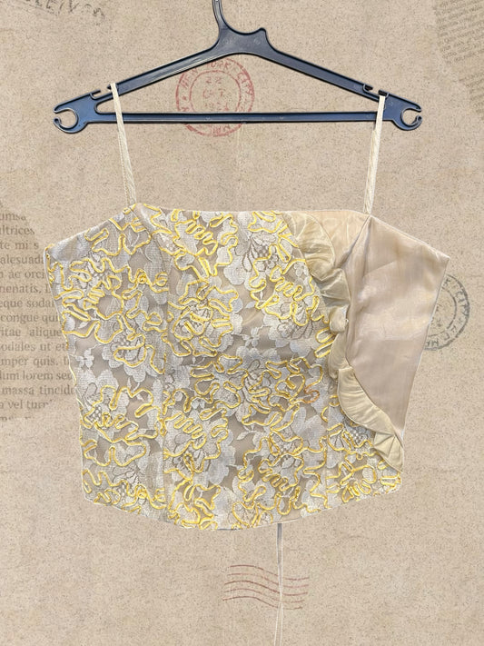 Romantic ivory corset top with floral lace and yellow embroidery. Features delicate straps, satin ruffles, and adjustable back ties. A dreamy vintage-inspired statement piece.