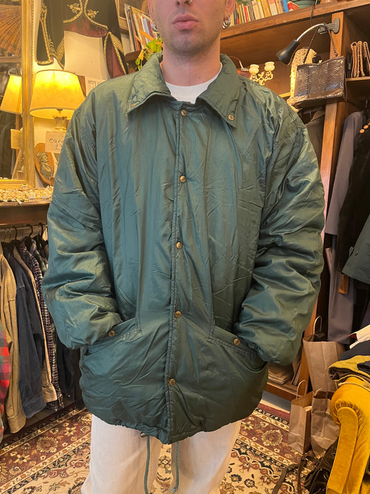 Vintage forest-green padded jacket with a relaxed oversized fit, classic collar, and subtle sheen for a clean retro outdoor aesthetic. Features brass-tone snap buttons, roomy front pockets, elasticated cuffs, and an adjustable drawstring hem
