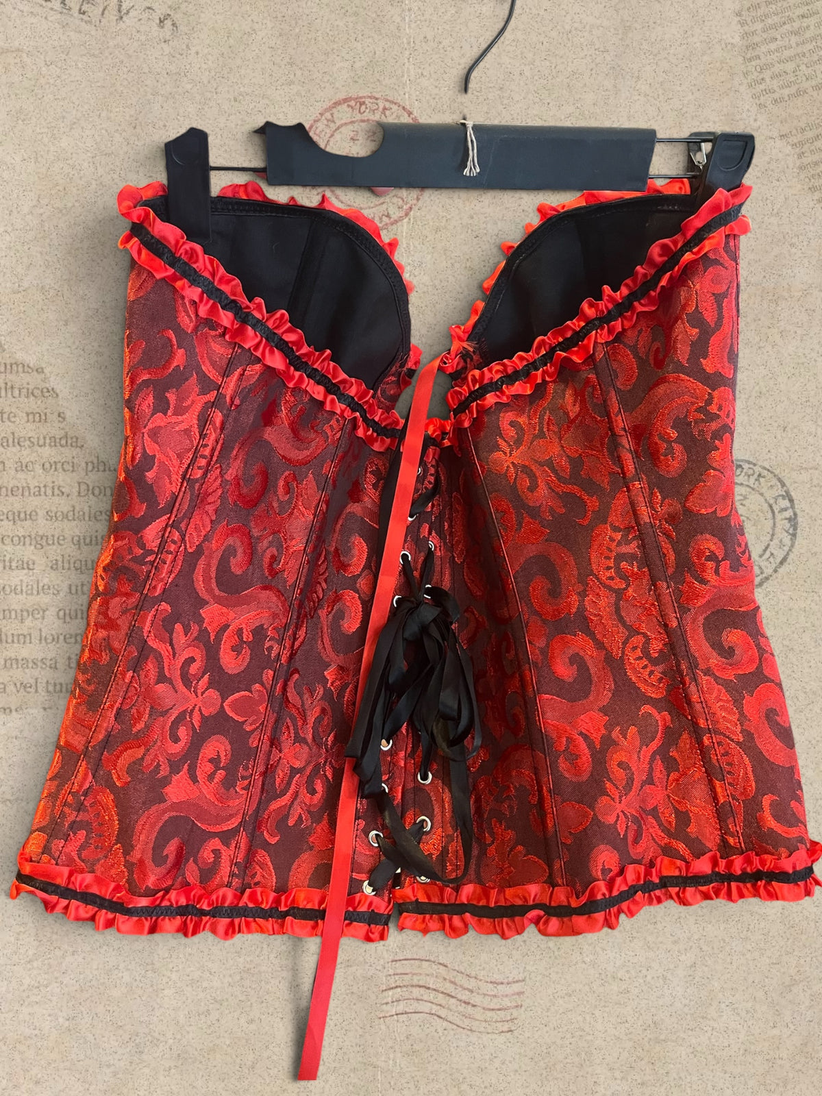 Victorian-inspired red corset with intricate brocade patterns and satin ruffles. Features front hook closure and a flattering, structured silhouette. A romantic statement piece with gothic elegance.