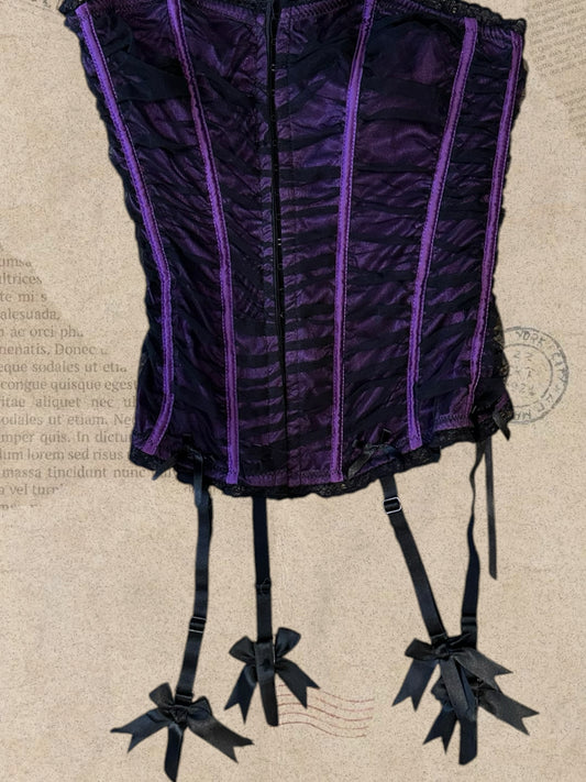 Gothic purple corset with black mesh detailing. Features adjustable lace-up back and garter straps with bows. A bold Victorian-inspired statement piece.