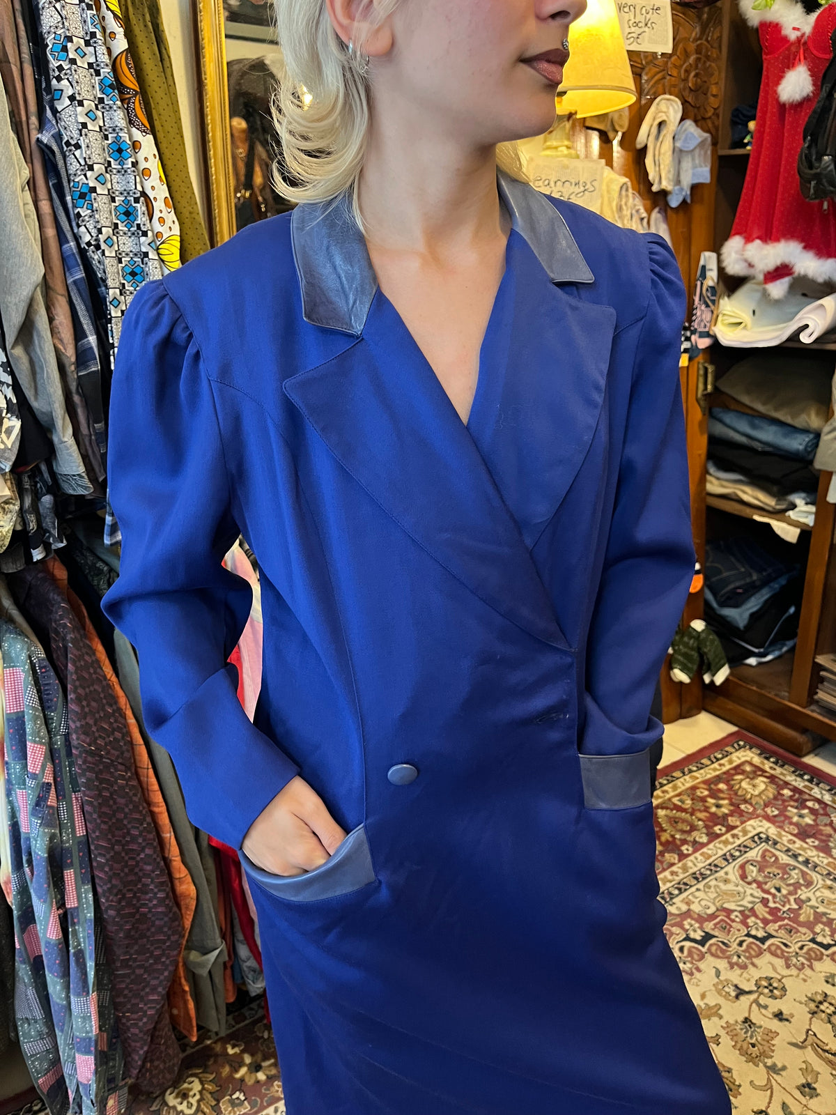 Vintage royal blue midi dress with a structured blazer-style silhouette and elegant puffed shoulders. Contrasting satin-effect collar and pocket details add a sophisticated retro touch.
