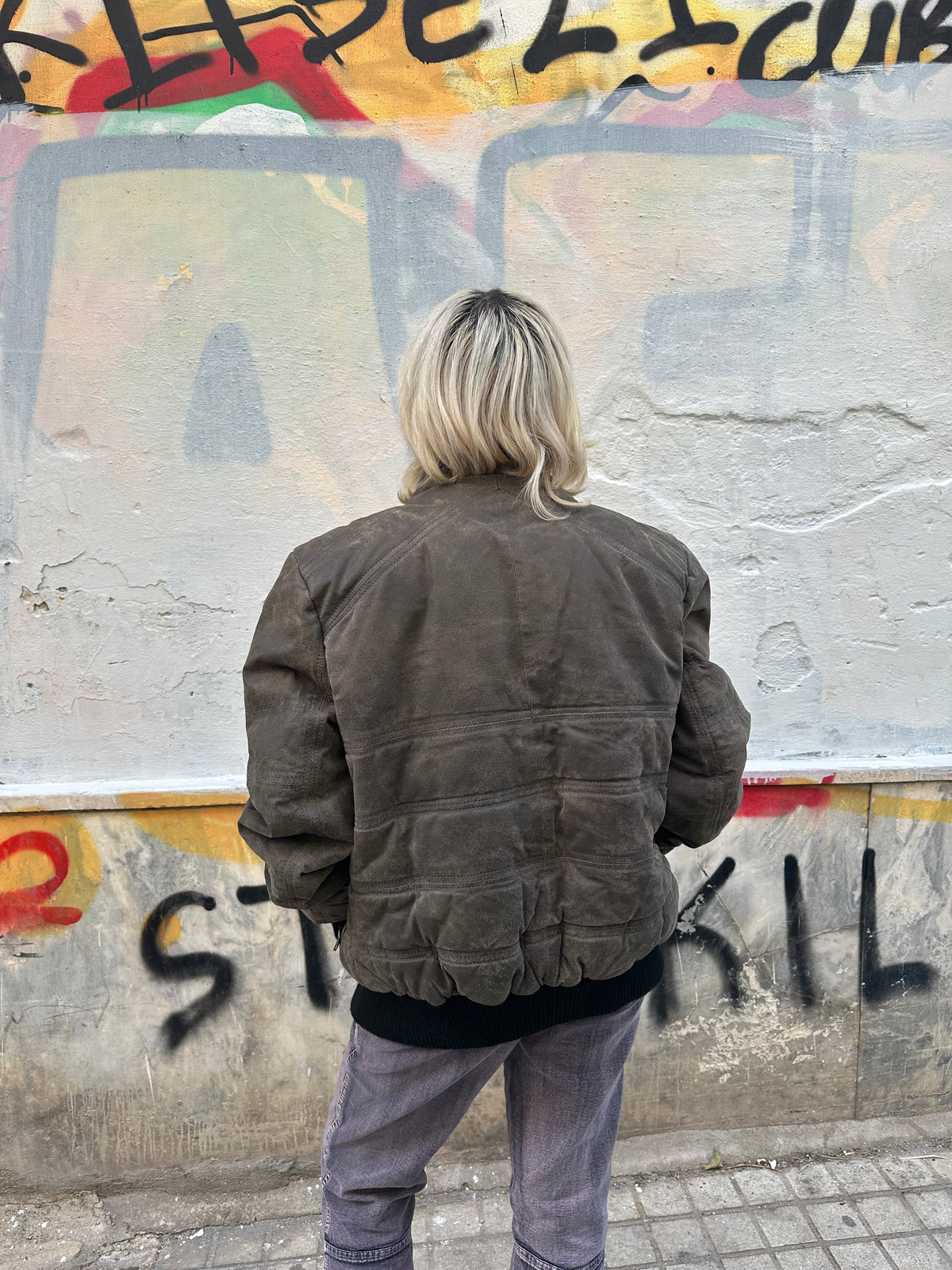Vintage taupe suede bomber jacket with an oversized fit and distressed finish.
Black ribbed details, high collar, and a bold 80s/90s utility aesthetic.