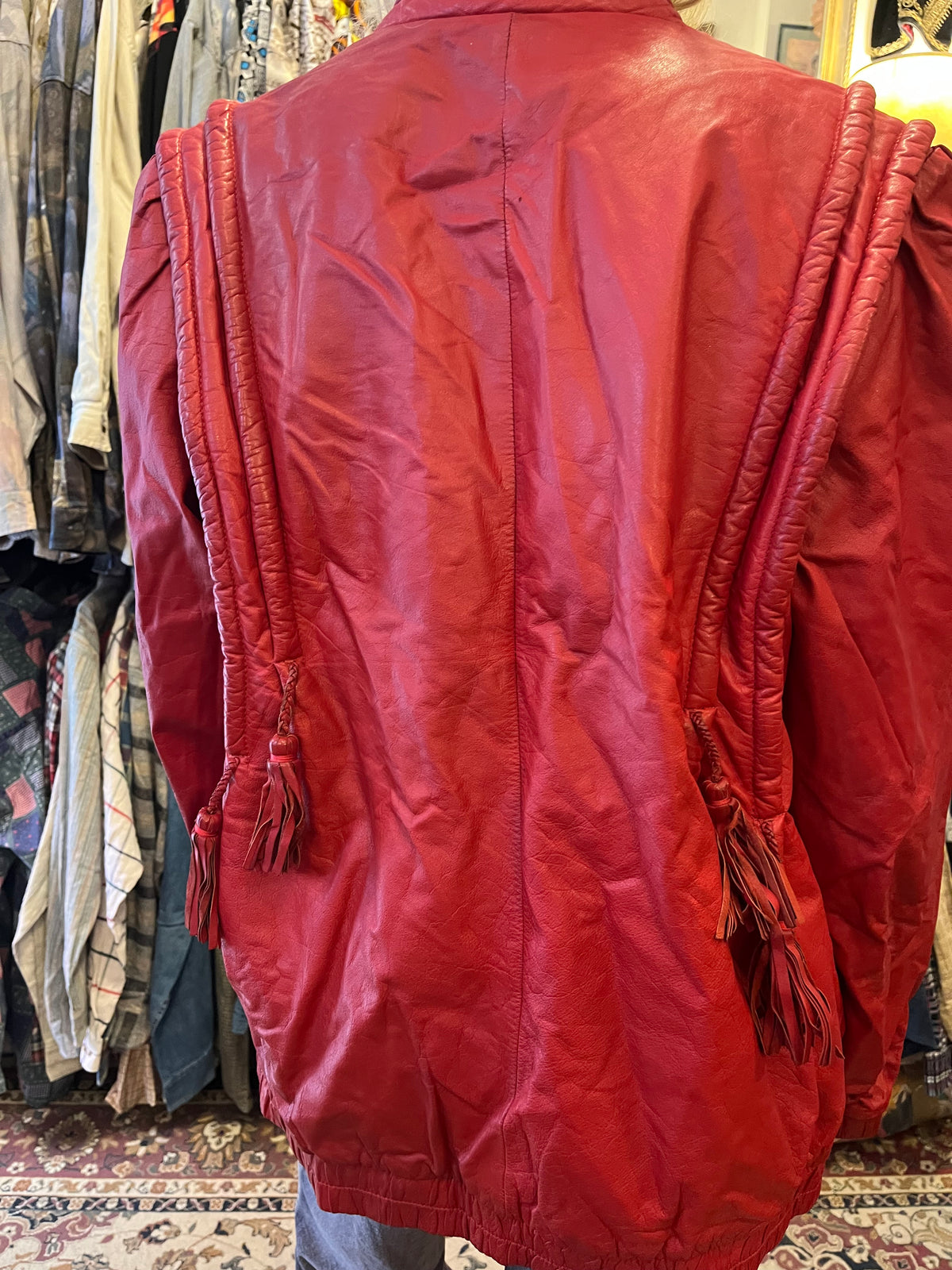 Statement red leather jacket featuring sculptural braided detailing and playful tassel accents. A bold vintage piece with a relaxed silhouette, zip-front closure, and unmistakable 80s-inspired attitude.