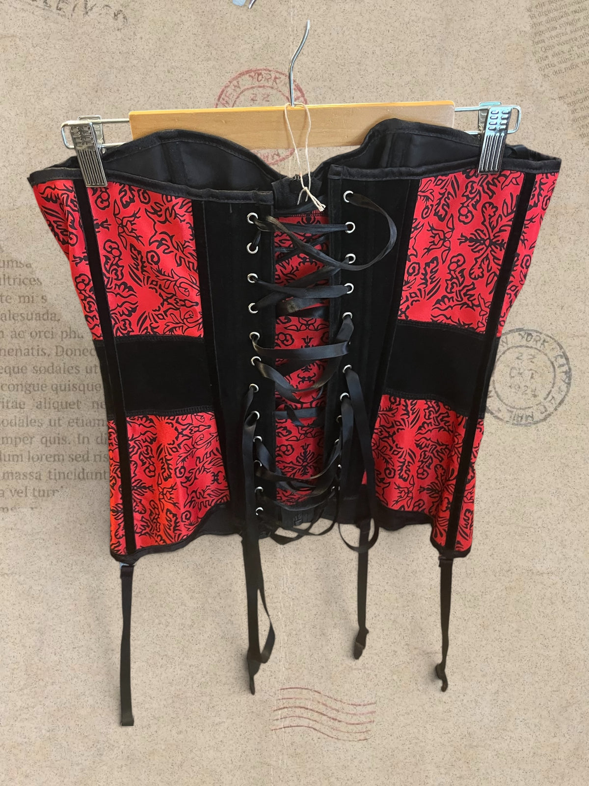 Gothic red and black corset with intricate floral patterns and a structured silhouette. Features adjustable lace-up back, front zipper, and garter straps. A bold Victorian-inspired statement piece.