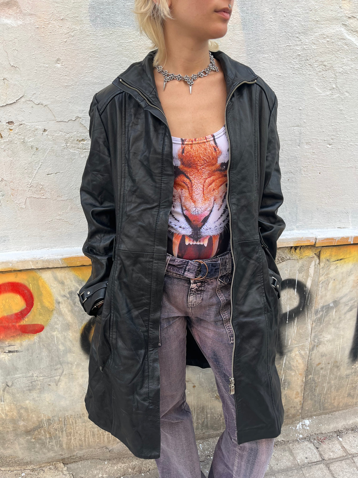 Long black leather coat with a sleek fitted silhouette, full zip closure, and buckle details at the cuffs and back. A bold vintage statement piece with a timeless biker-inspired edge.