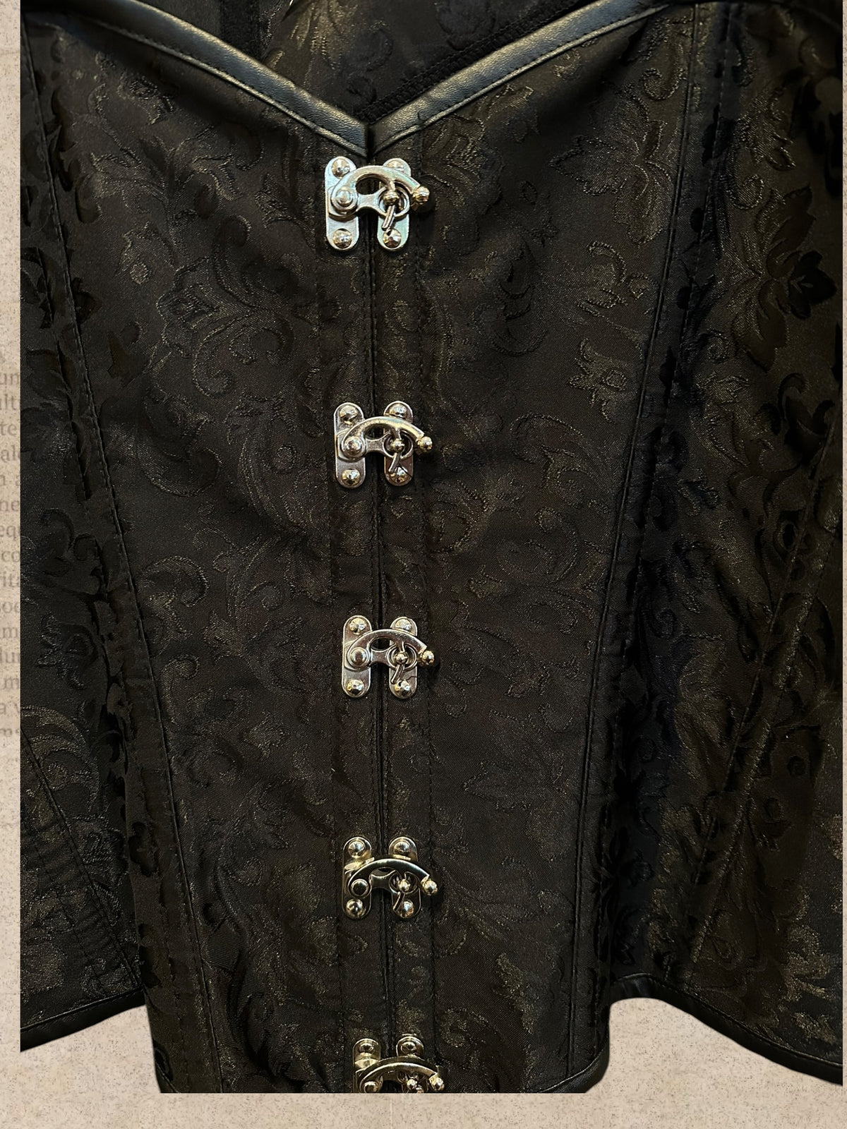 Black brocade corset with elegant floral patterns. Silver clasps, buckle straps and adjustable lace-up back. A bold gothic Victorian statement piece.