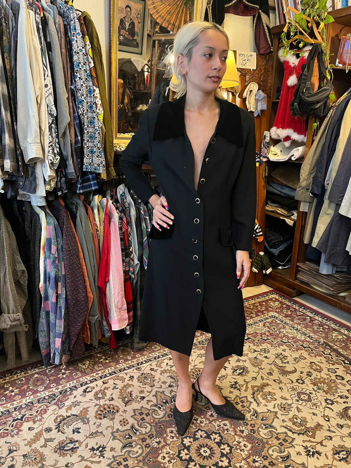 Elegant vintage black midi coat dress featuring a statement velvet collar and gold-tone buttons. Tailored silhouette with velvet pocket details for a timeless, sophisticated look.