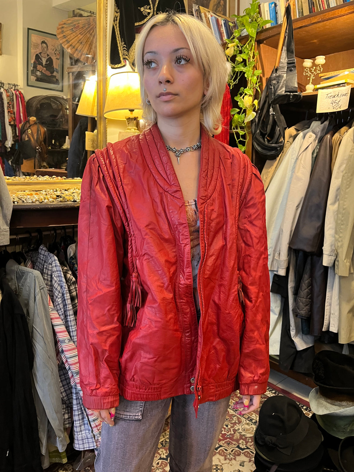 Statement red leather jacket featuring sculptural braided detailing and playful tassel accents. A bold vintage piece with a relaxed silhouette, zip-front closure, and unmistakable 80s-inspired attitude.